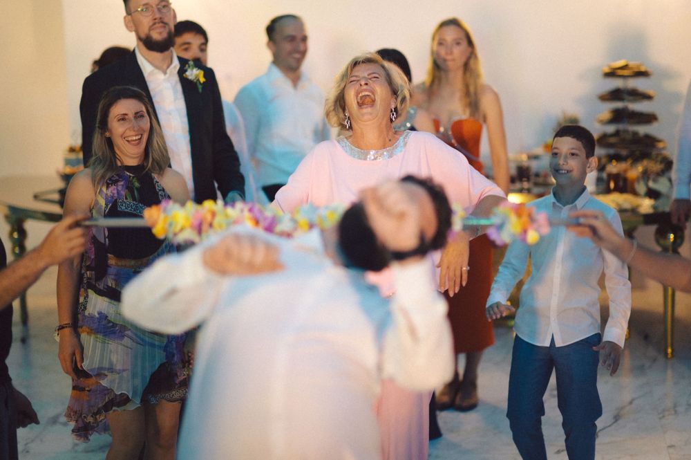 Guests laughing and dancing with flower garlands at lively celebration party.