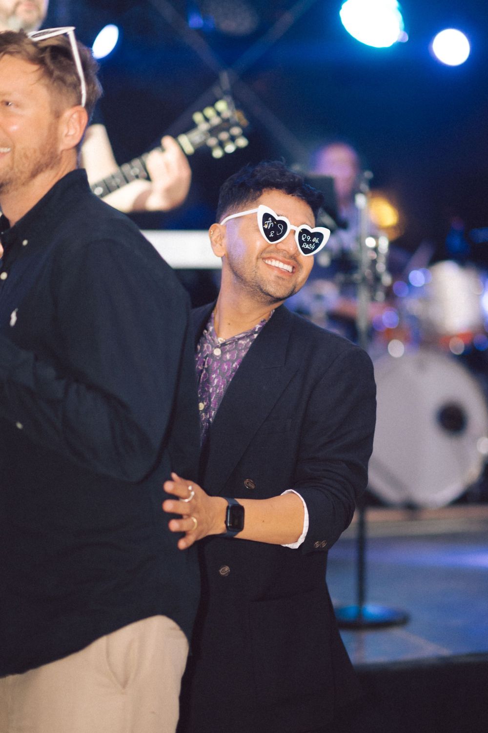 Guest wearing heart-shaped sunglasses dancing near band setup with blue stage lighting.