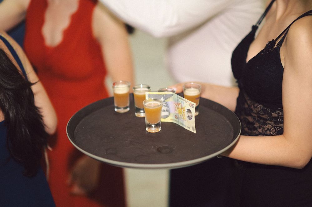 Serving tray with shot glasses and cash tip being carried at party event.