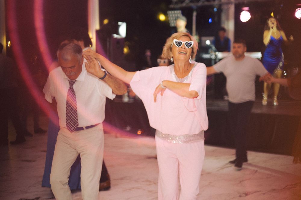 People dancing energetically at a party with colorful lighting in the background.
