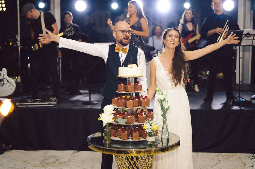 Newlyweds posing triumphantly next to their multi-tiered wedding cake.