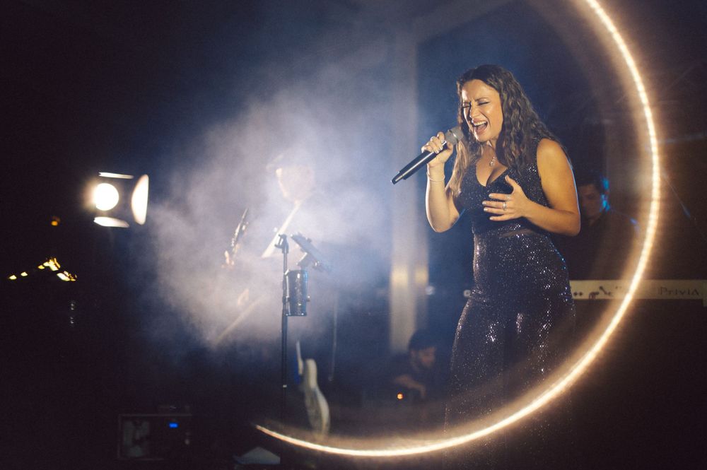 Concert performance with singer silhouetted against curved lighting and atmospheric smoke.