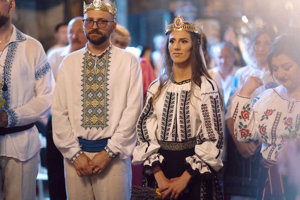 Orthodox wedding ceremony with crowned couple in traditional embroidered attire.