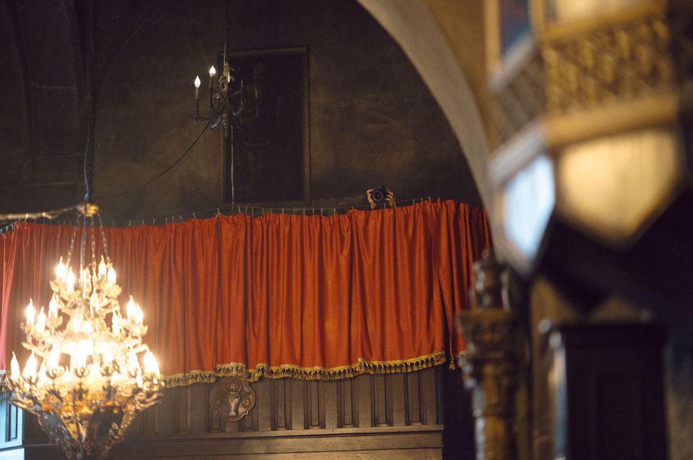 Elegant crystal chandelier hanging in church with red curtain backdrop.