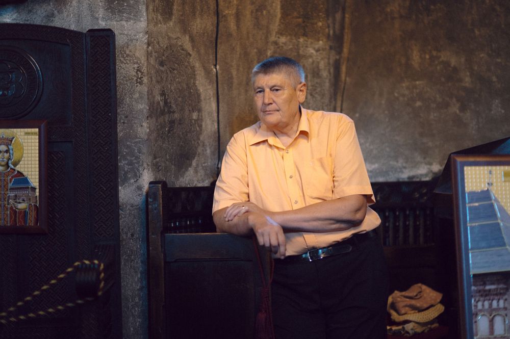 A person in an orange shirt sits in a wooden church pew against a stone wall.