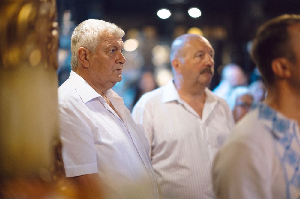 Attendees stand during an Orthodox church service in traditional white clothing.