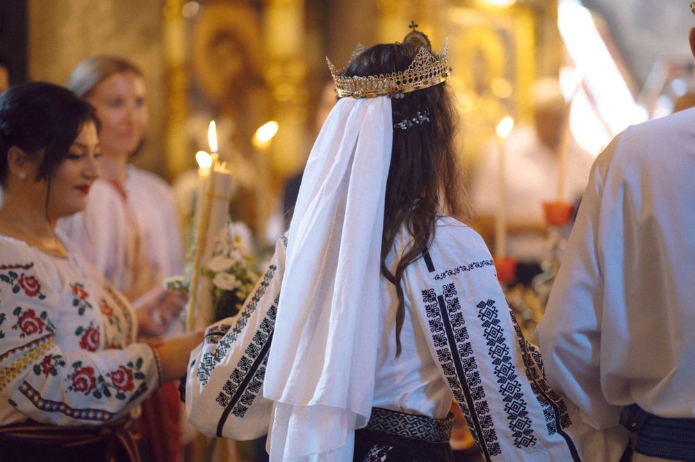 A wedding ceremony participant wearing traditional Romanian folk costume with embroidery and ceremonial crown.
