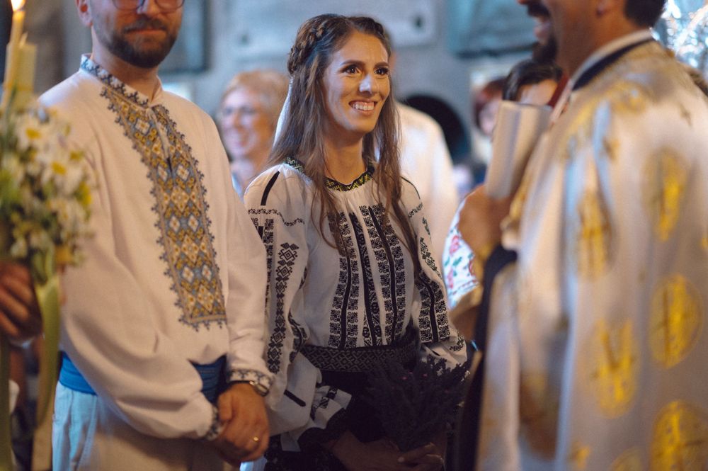 A person wearing an ornate embroidered blouse stands among others at a cultural gathering.