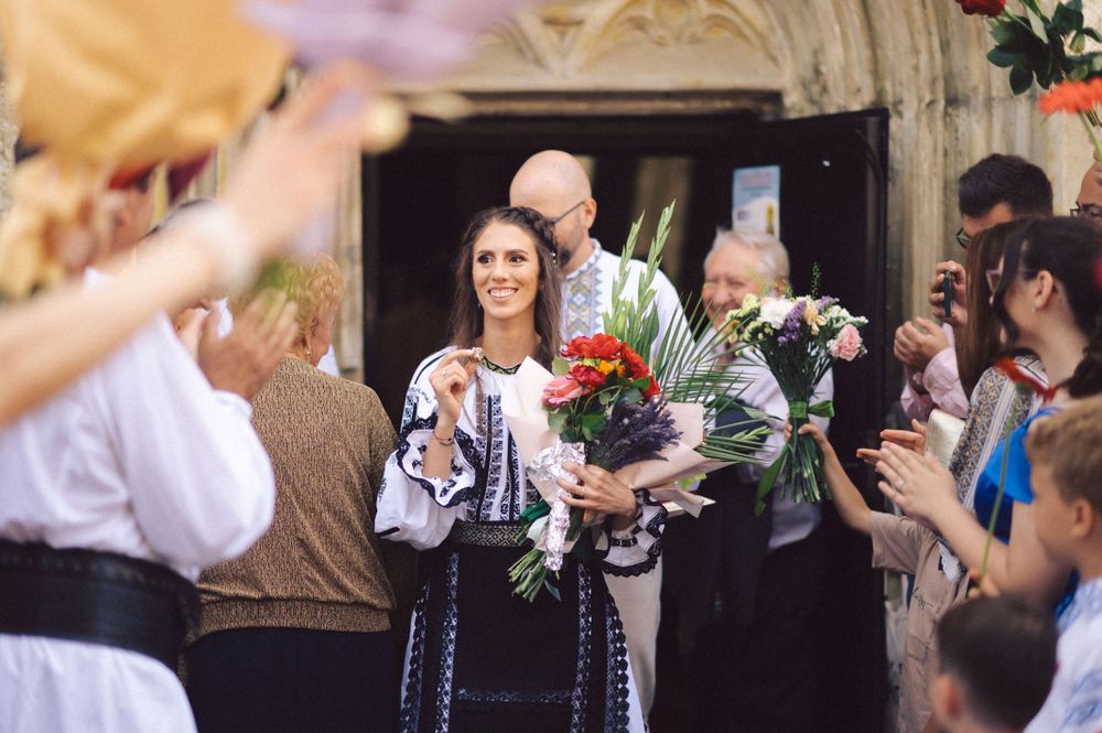 Someone holding flowers and wearing traditional embroidered clothing stands among a crowd.