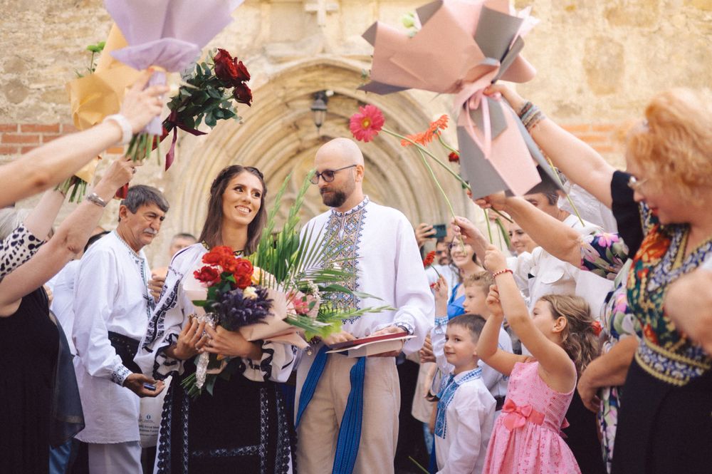 People hold up flowers in celebration as a couple stands beneath at an outdoor gathering.