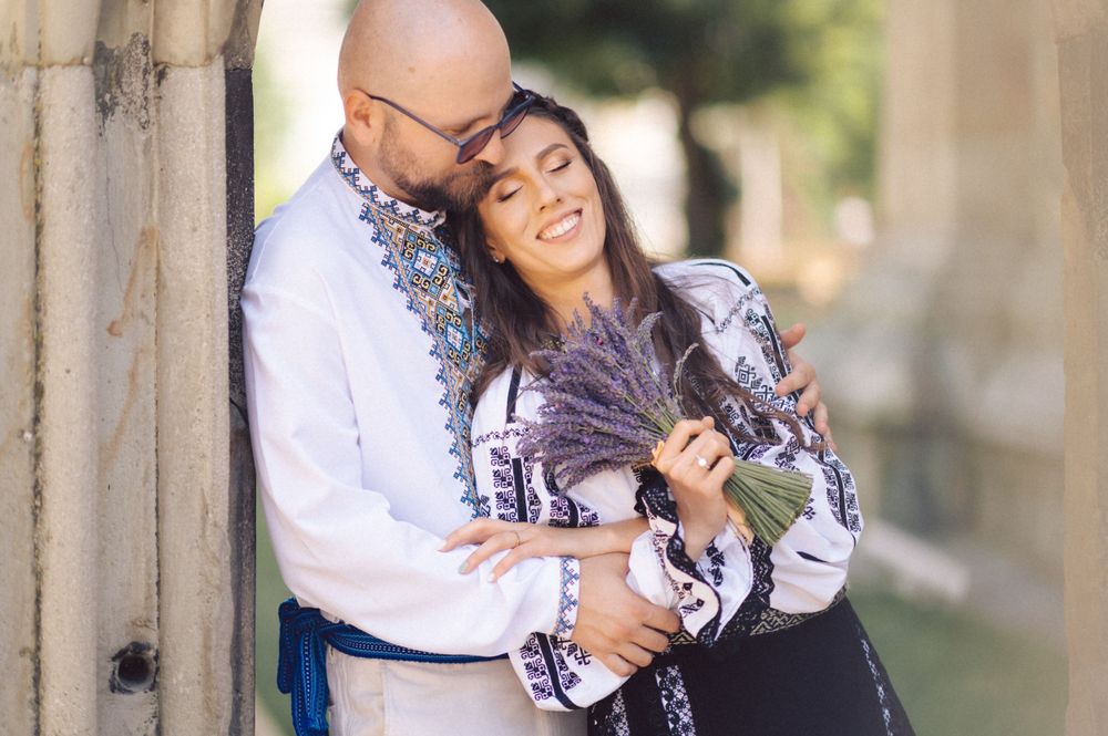 A romantic moment between a couple wearing traditional Romanian outfits near a stone wall.