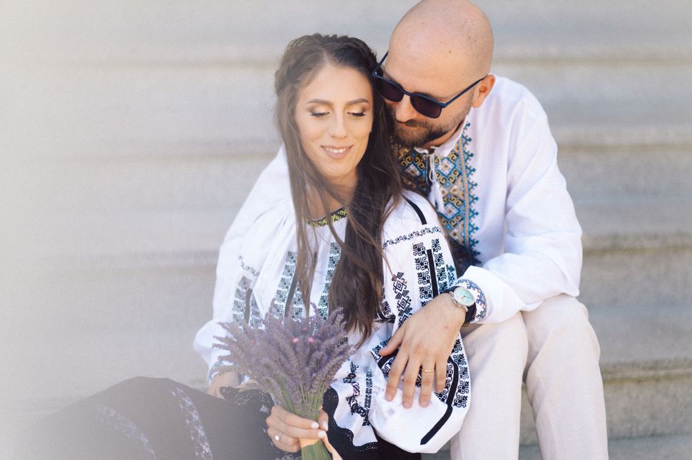 A couple in traditional Romanian attire shares an intimate moment on stone steps.