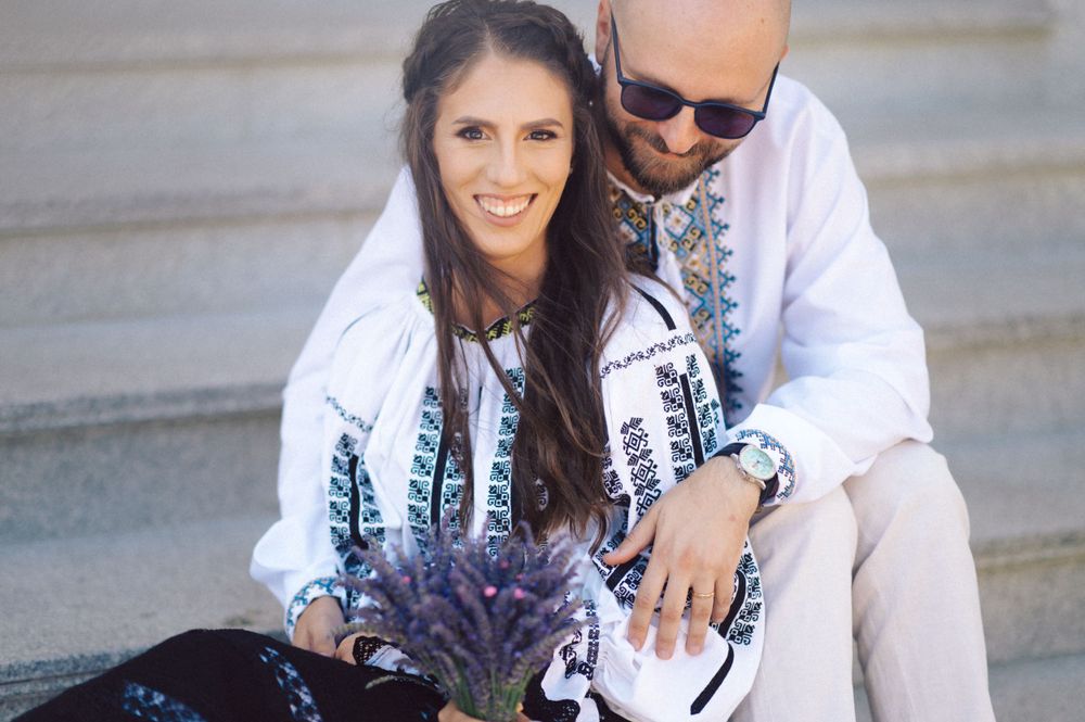A couple in traditional Romanian clothing poses with lavender on stone steps.