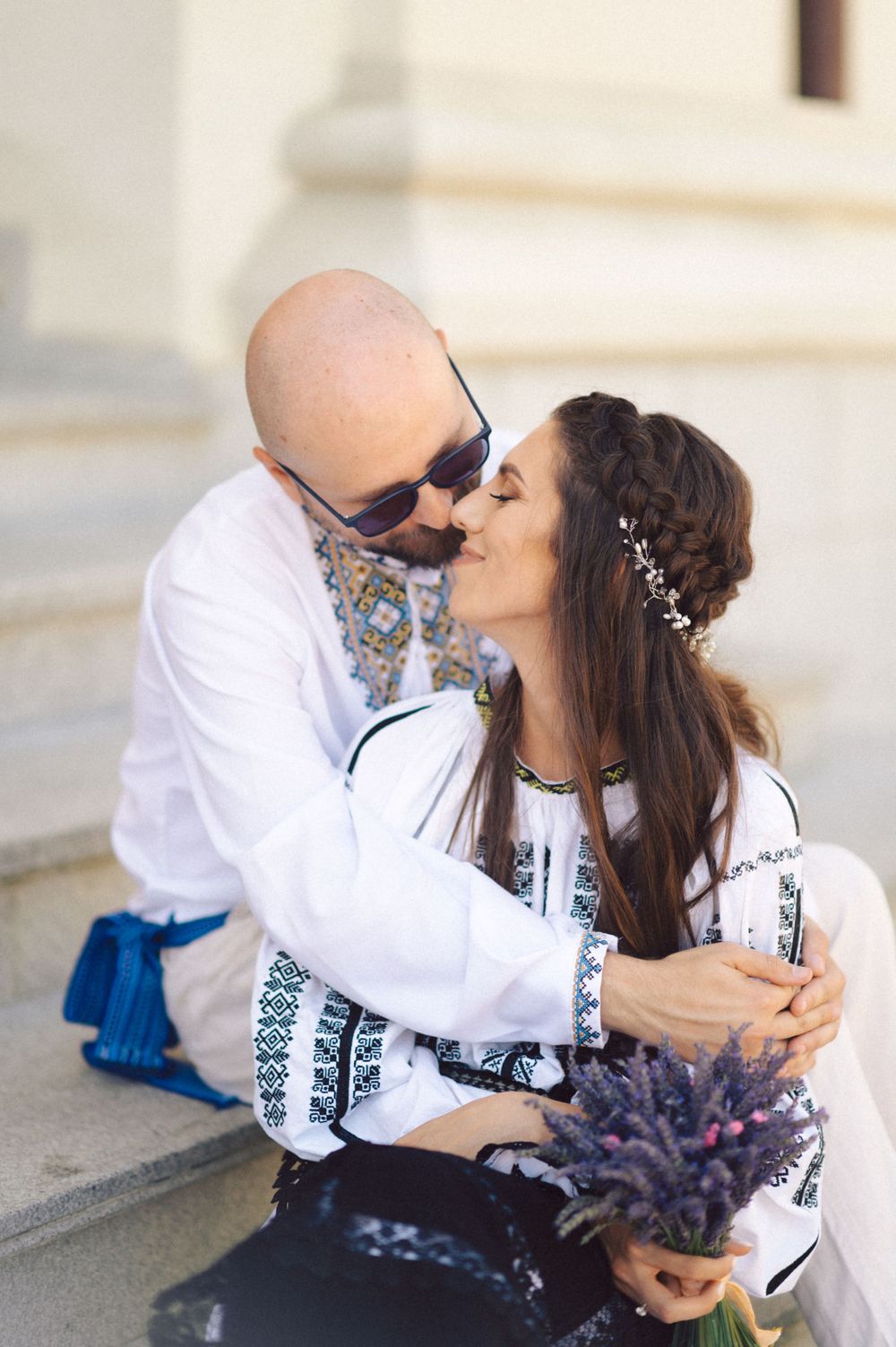 A couple in traditional Romanian attire sharing a romantic moment on stone steps with lavender flowers.