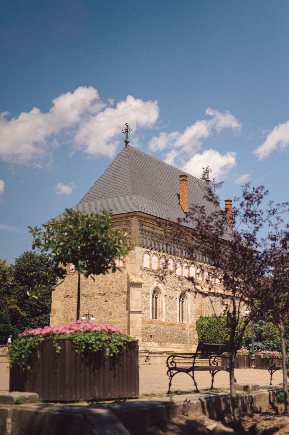 Historic stone church building with ornate architecture and a decorative bench under blue skies.