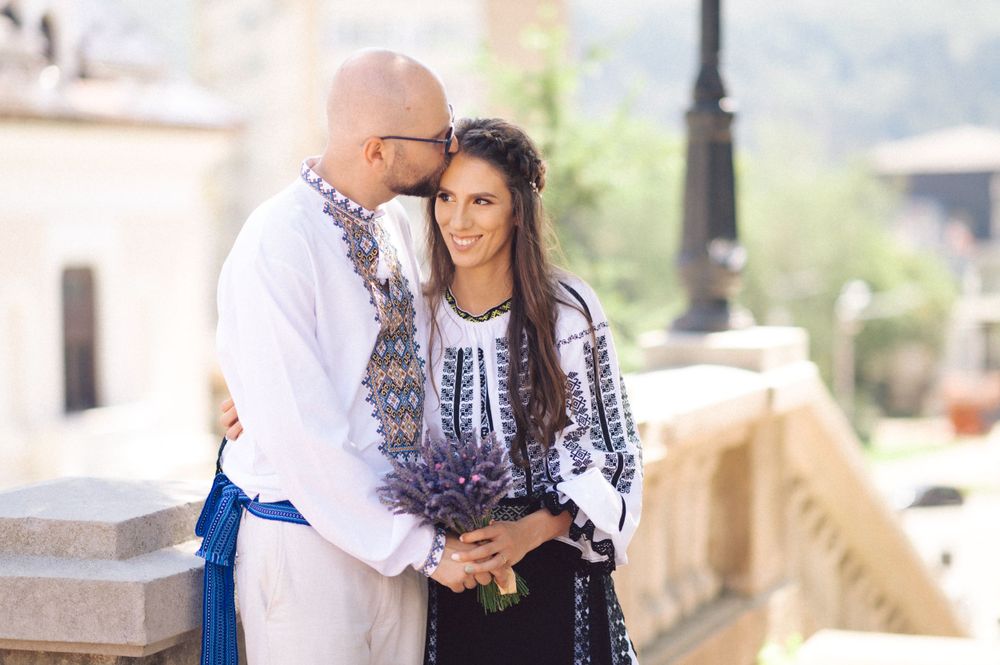 A couple in traditional Romanian folk dress embracing on a sunny terrace.