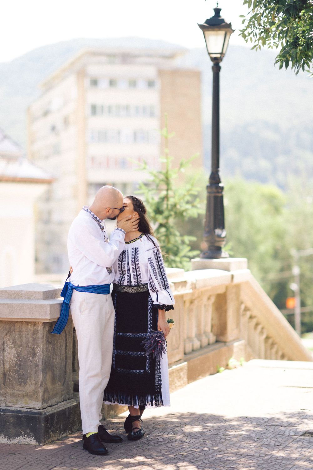 A couple in traditional Romanian clothing sharing an intimate moment near a vintage lamppost.