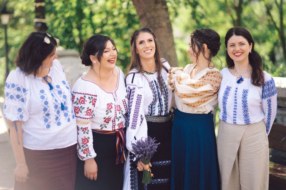Friends laughing together while wearing traditional Romanian folk blouses with colorful embroidery.