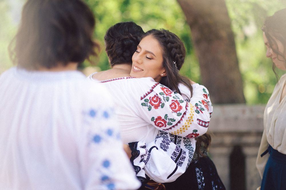 People in traditional Romanian folk costumes embracing during an outdoor gathering.
