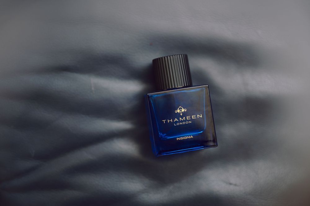 Blue glass perfume bottle photographed against dark shadows on gray background.