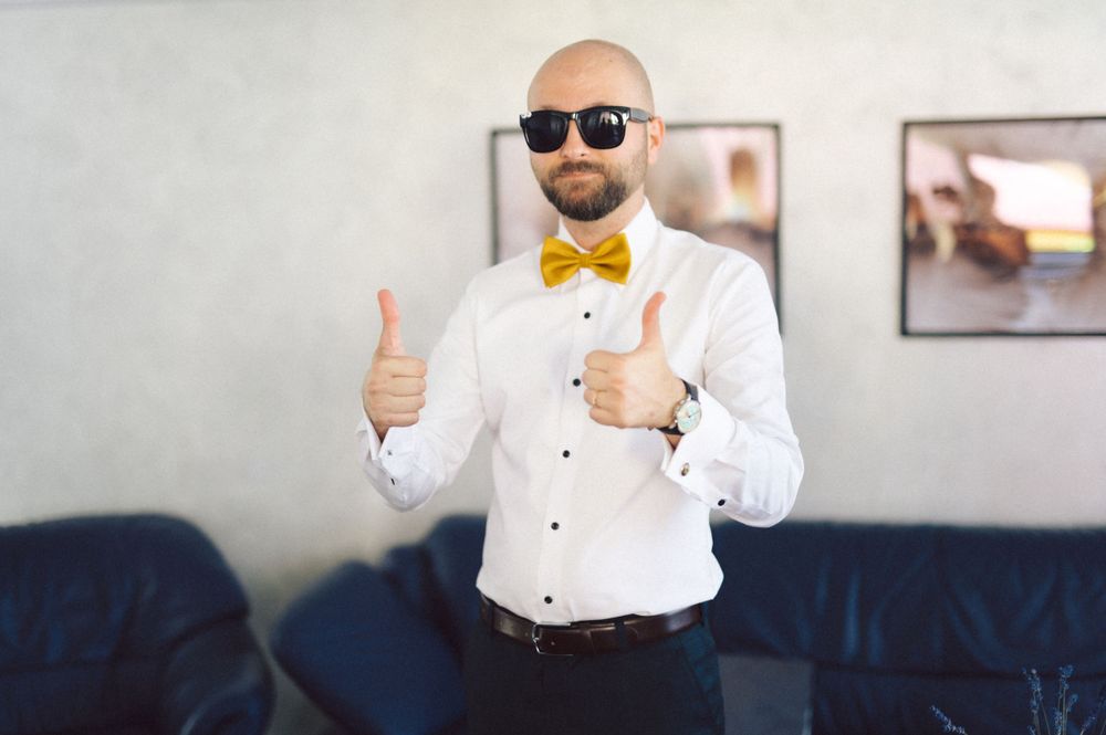Formal outfit with yellow bowtie and sunglasses giving thumbs up gesture.