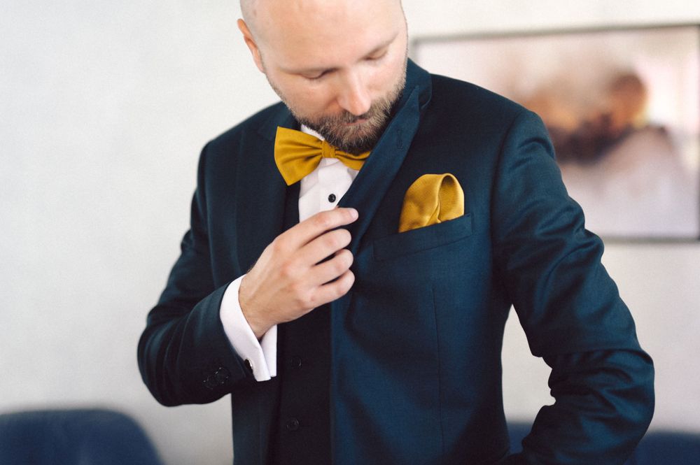 Navy suit jacket with yellow bowtie and matching pocket square being adjusted.