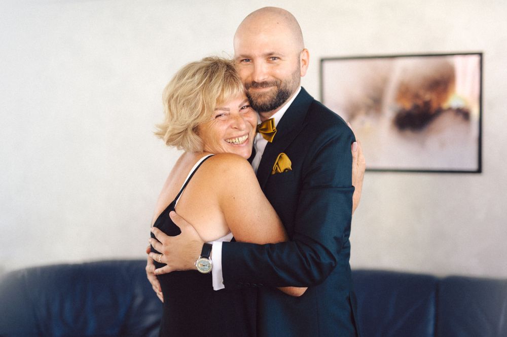 A romantic couple embraces during their wedding photoshoot on a blue couch with artwork in the background.