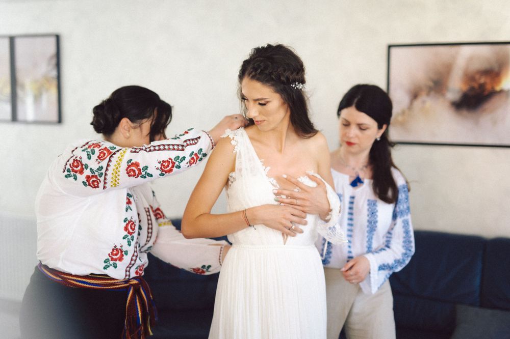 Women in traditional embroidered clothing help bride prepare in her wedding dress.