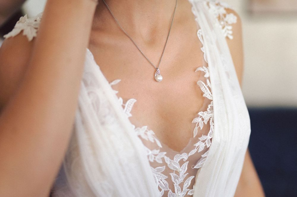 Close-up detail of delicate lace wedding dress neckline with pendant necklace.