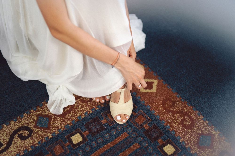 Close-up of bride's feet in white sandals on ornate patterned rug.