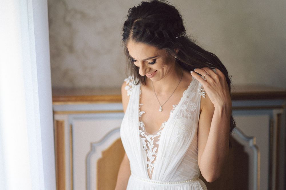 Person in a delicate white lace wedding gown adjusts their hair in soft lighting.