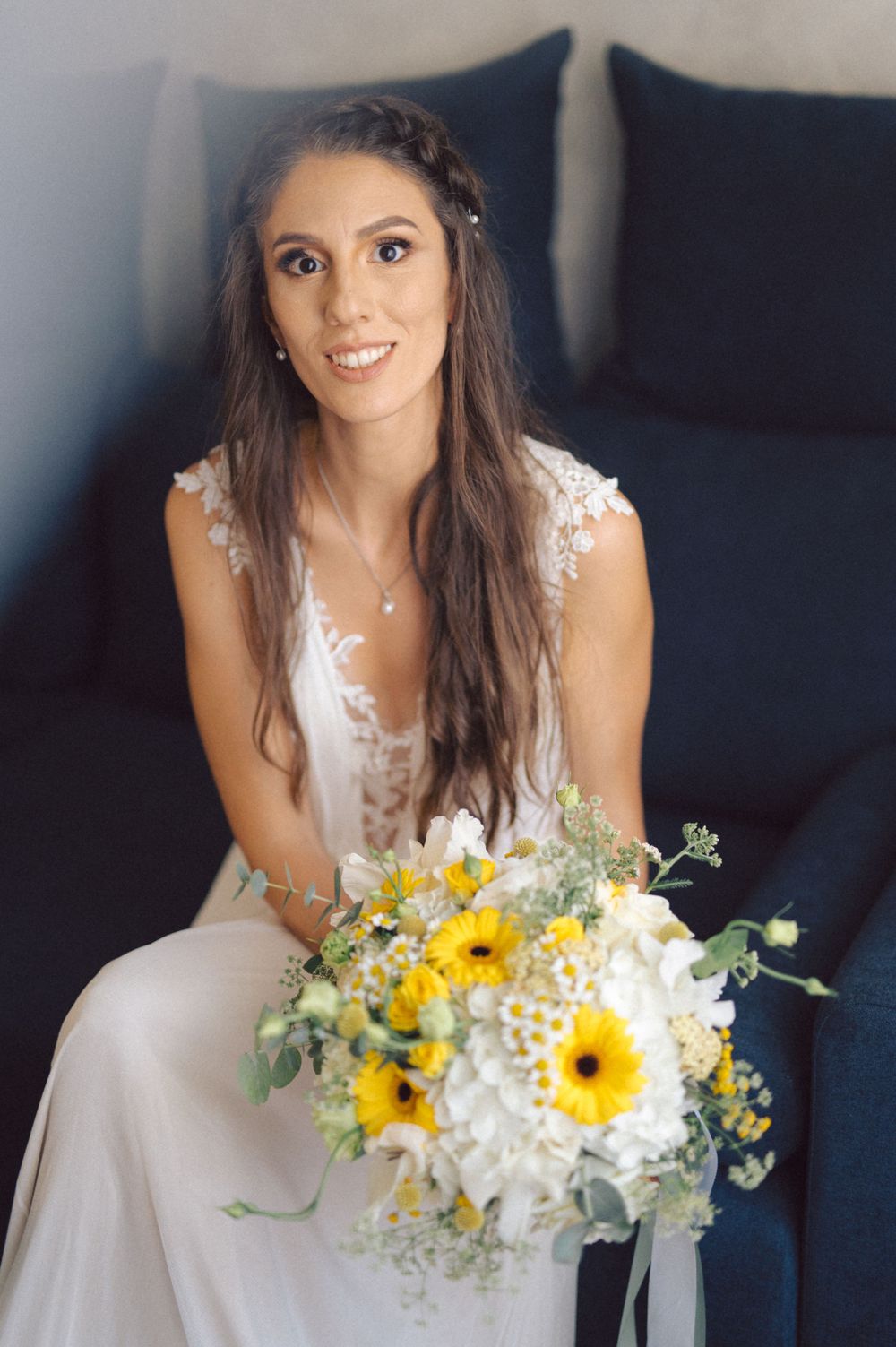 Person in white wedding dress holds beautiful bouquet with yellow sunflowers and greenery.