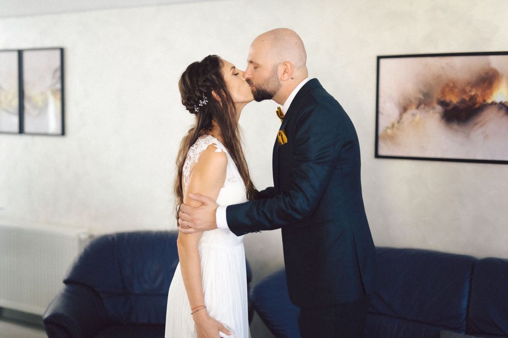 Couple sharing a romantic kiss during their wedding, with art prints visible on the wall behind them.