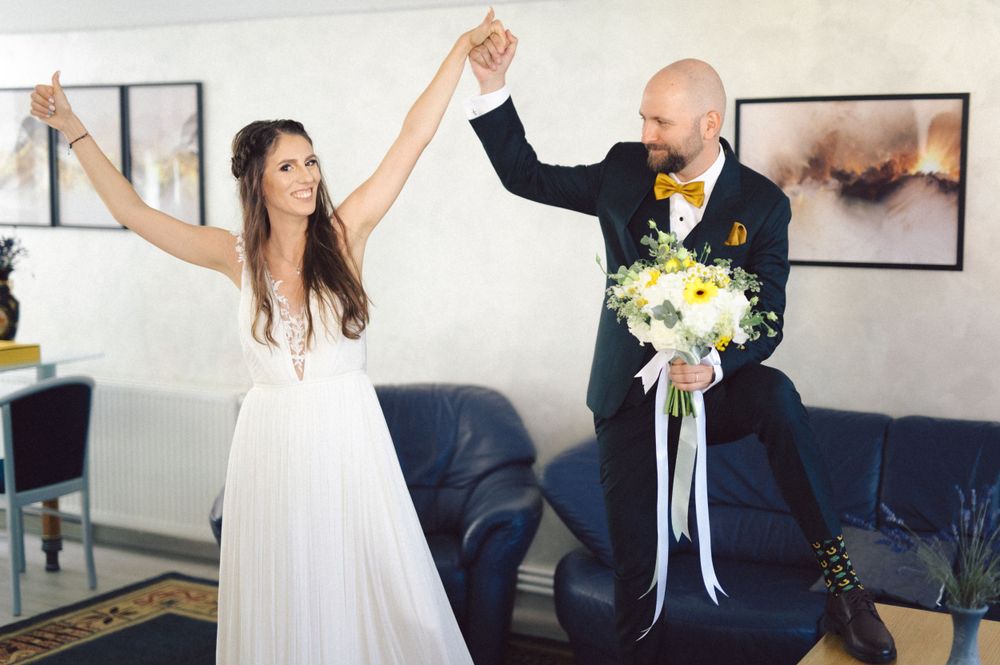 Joyful couple raises their hands in celebration during wedding ceremony with floral bouquet.