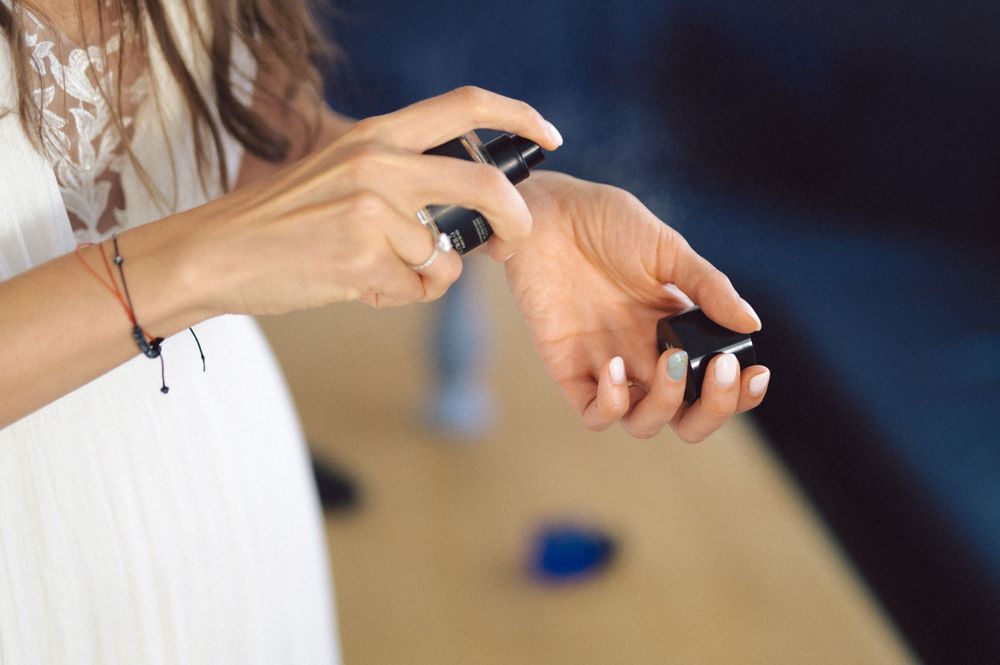 Hands spraying perfume onto wrists in an elegant white lace dress sleeve.