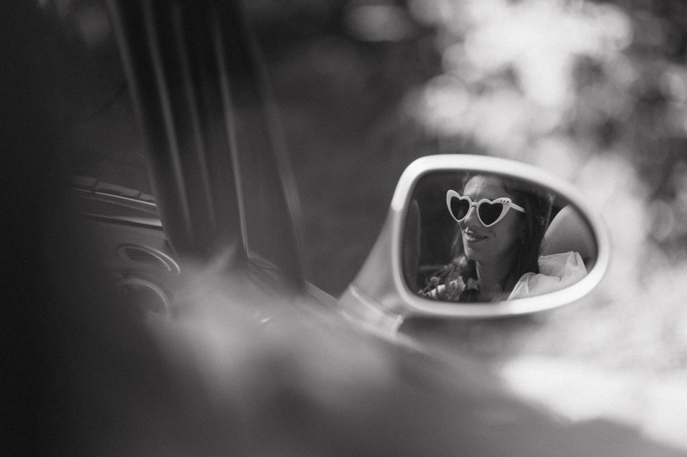 Artistic black and white reflection of sunglasses in a car side mirror.