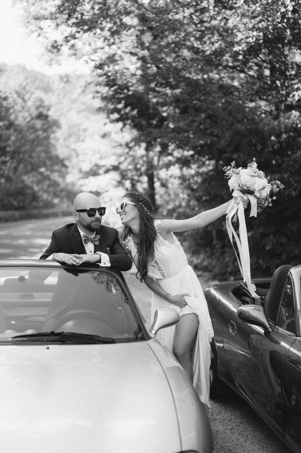 Black and white wedding photo with vintage cars and a romantic moment.