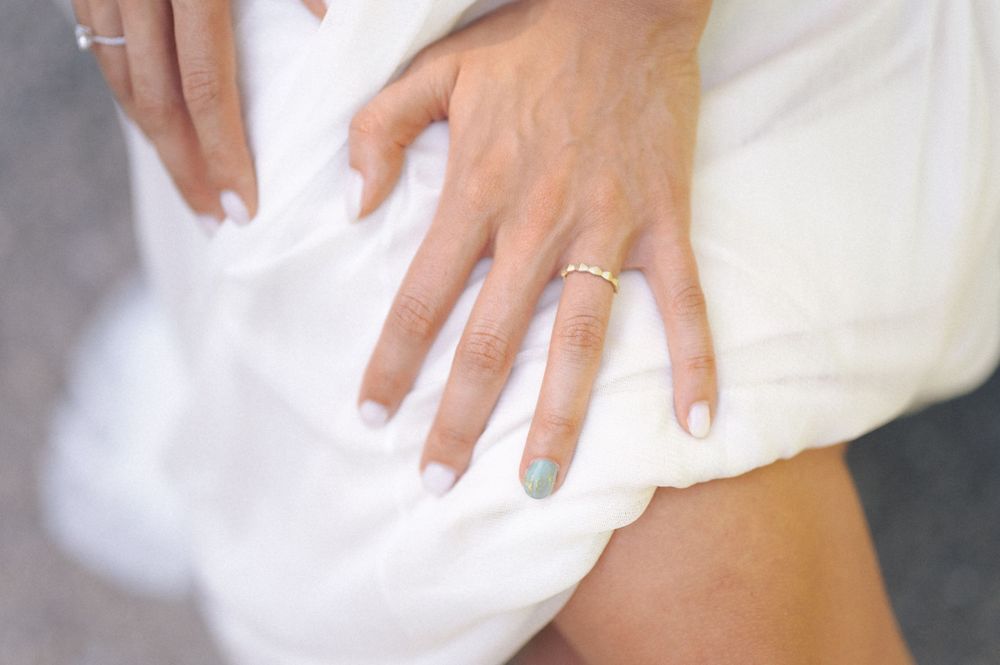 Close-up of a wedding ring and manicured nails against white fabric.