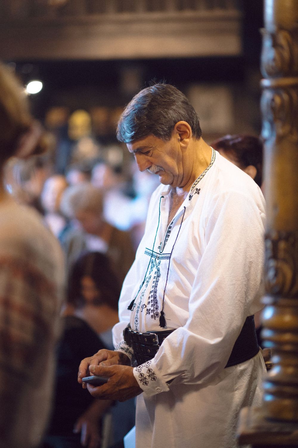 Person wearing traditional white embroidered clothing at an indoor gathering.