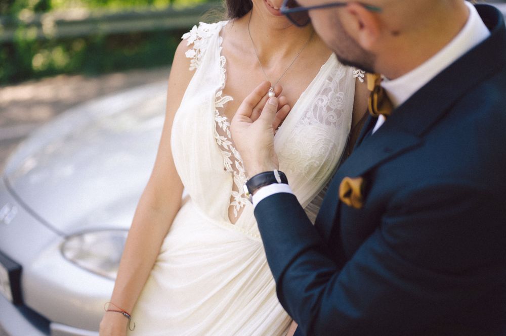 Intimate close-up of wedding couple near a silver car showing dress details.
