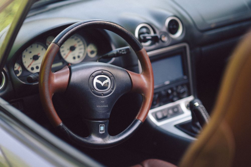 Interior view of a Mazda sports car showing wooden steering wheel and dashboard controls.