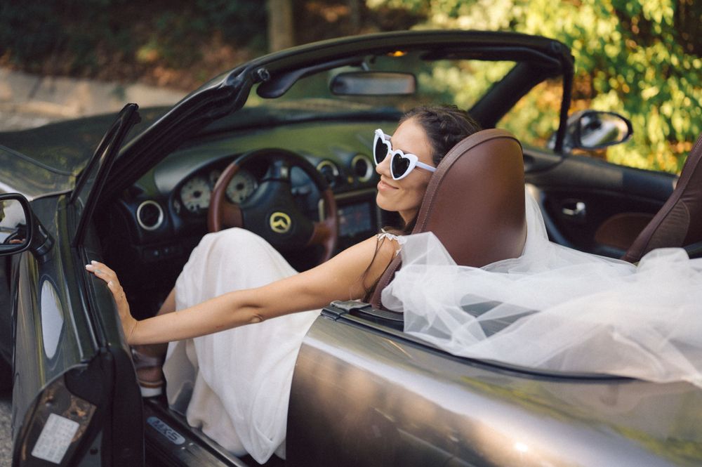 Driver in white dress and retro sunglasses enjoying a convertible ride.