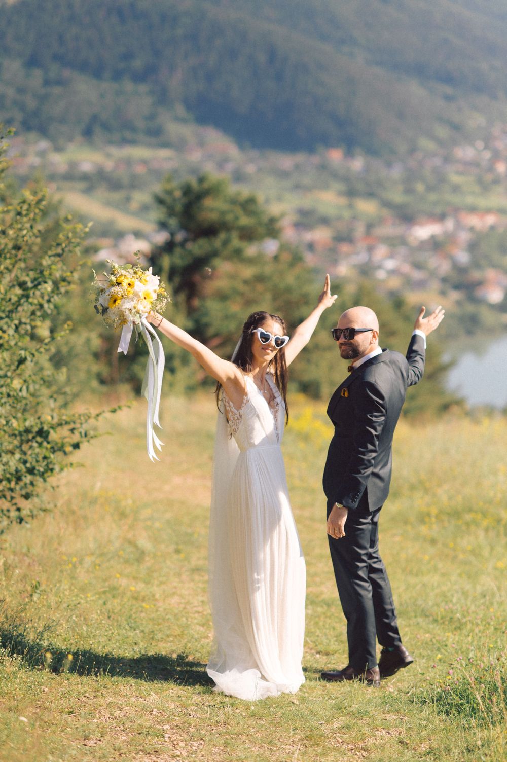 Joyful wedding couple celebrating on a hilltop overlooking a scenic mountain valley.