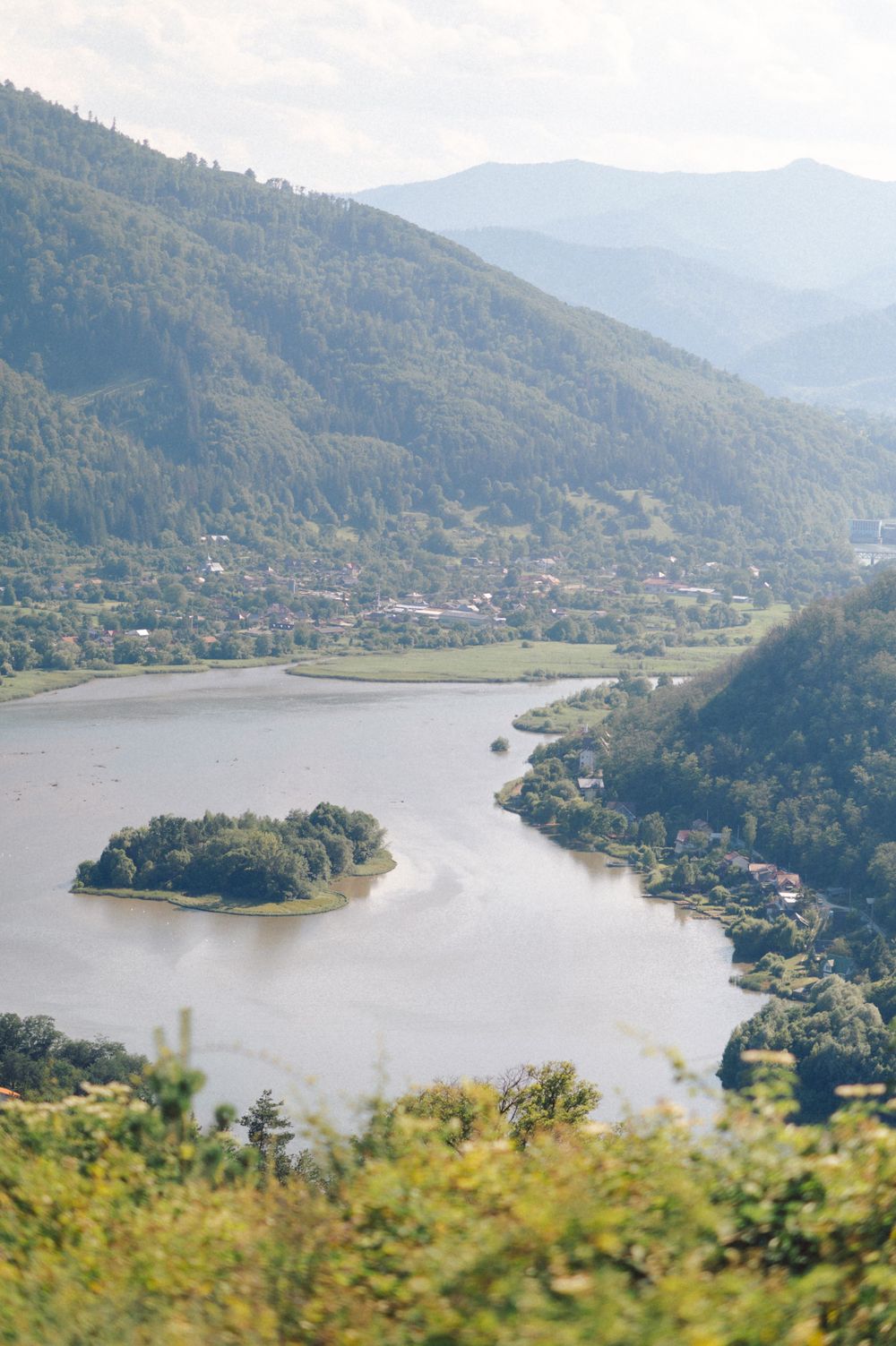 Scenic mountain landscape with a lake and small island surrounded by forested hills.
