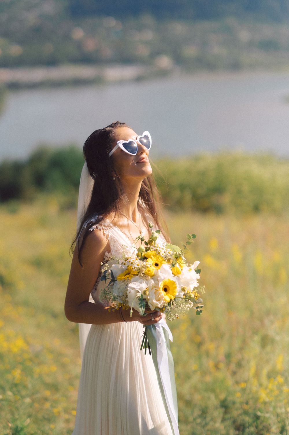 Bride in white dress holding yellow bouquet against mountain backdrop.