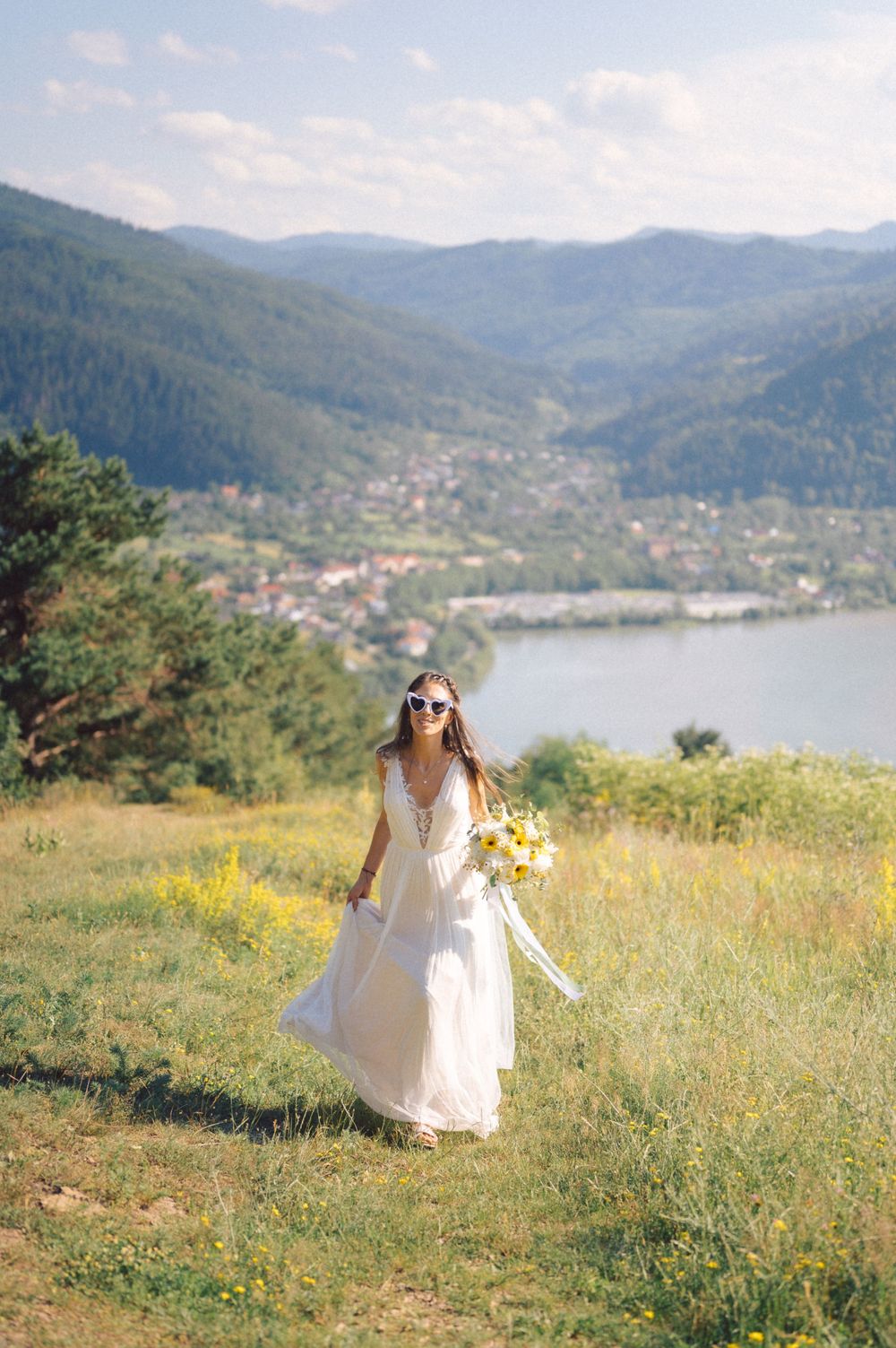 Elegant bride walking through wildflower meadow with mountain lake vista.