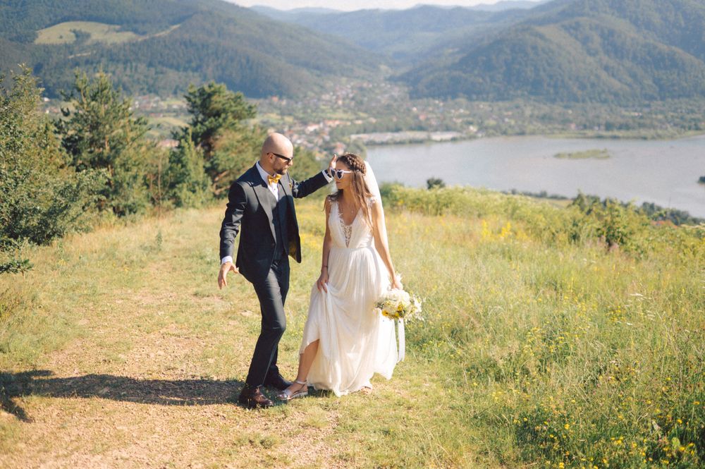 Wedding couple walks along mountain trail with lake view in the background.