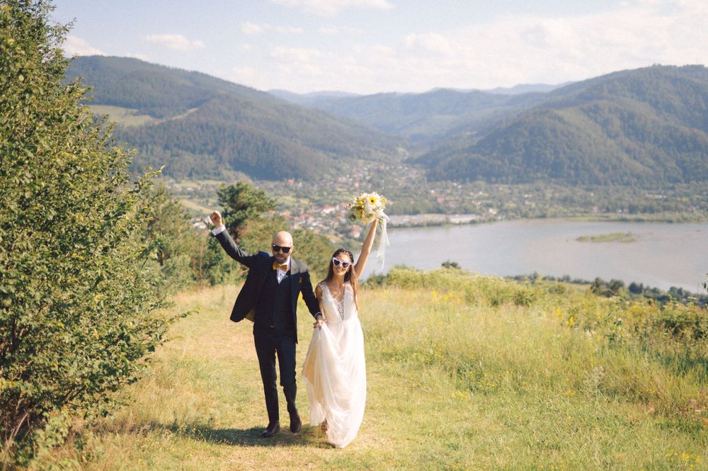 Joyful wedding couple celebrates on hilltop overlooking mountain lake landscape.