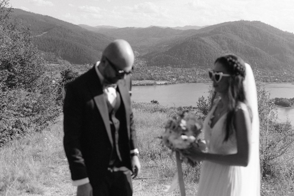 Black and white wedding portrait with mountain lake scenery in background.