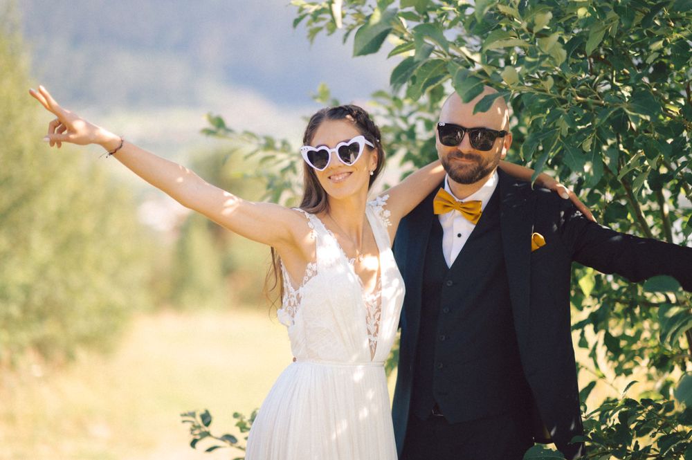 Wedding couple in sunglasses strikes fun pose against mountain landscape.